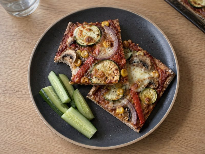 Fuldkornspizza med grønt på en mørk tallerken, set ovenfra