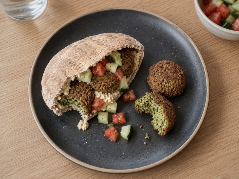 Ovnbagte falafler med pitabrød, hummus og grønt på en mørk tallerken, set ovenfra