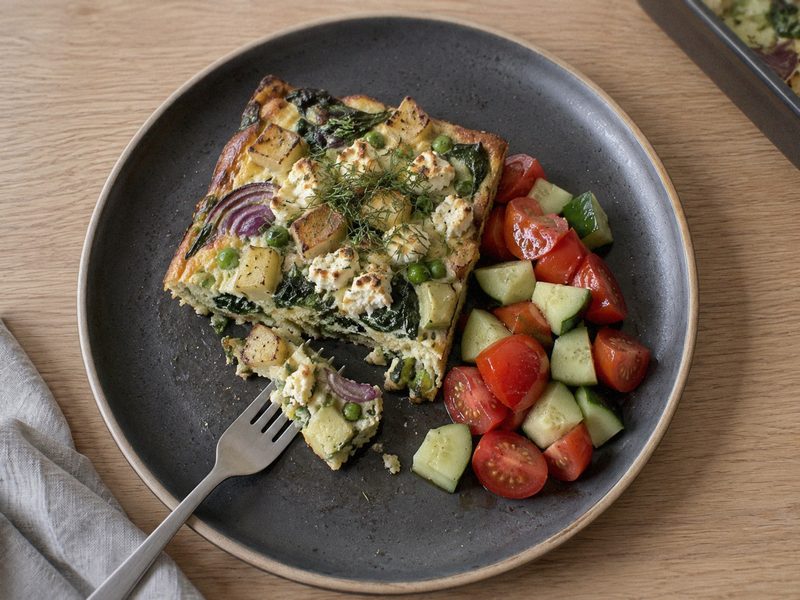 Ovnfrittata med kartofler, ærter og feta på en mørk tallerken, set ovenfra