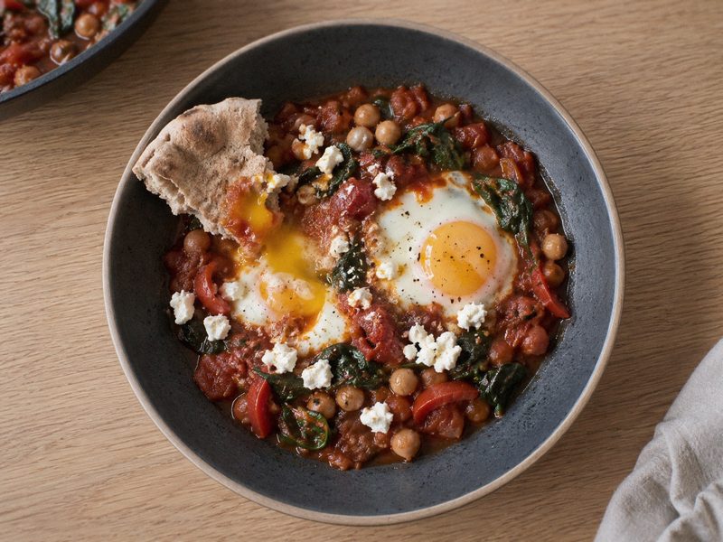 Shakshuka med kikærter og spinat på en mørk tallerken, set ovenfra